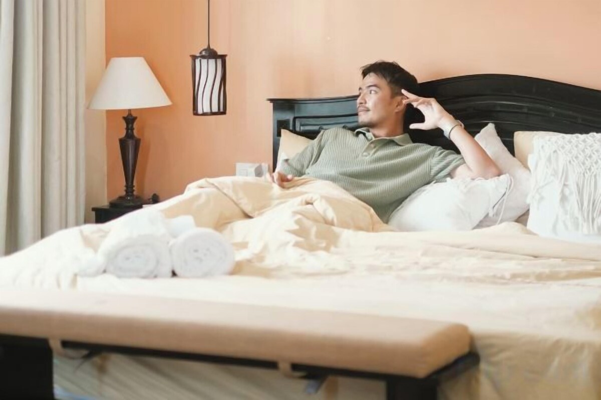 Una persona acostada en la cama con toallas enrolladas y una lámpara en la mesita de noche.