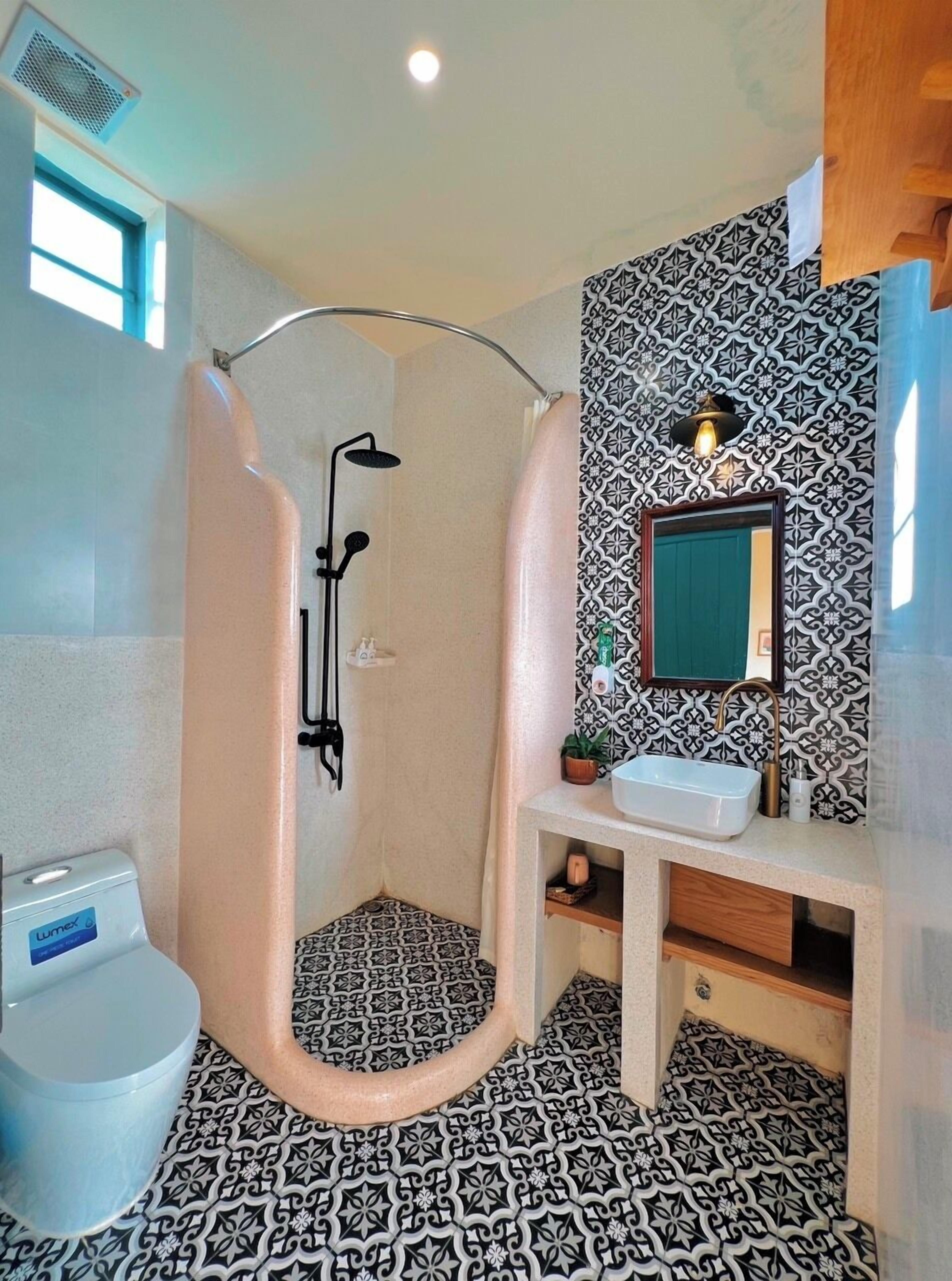 A bathroom with a shower, toilet, sink, and patterned tiles.