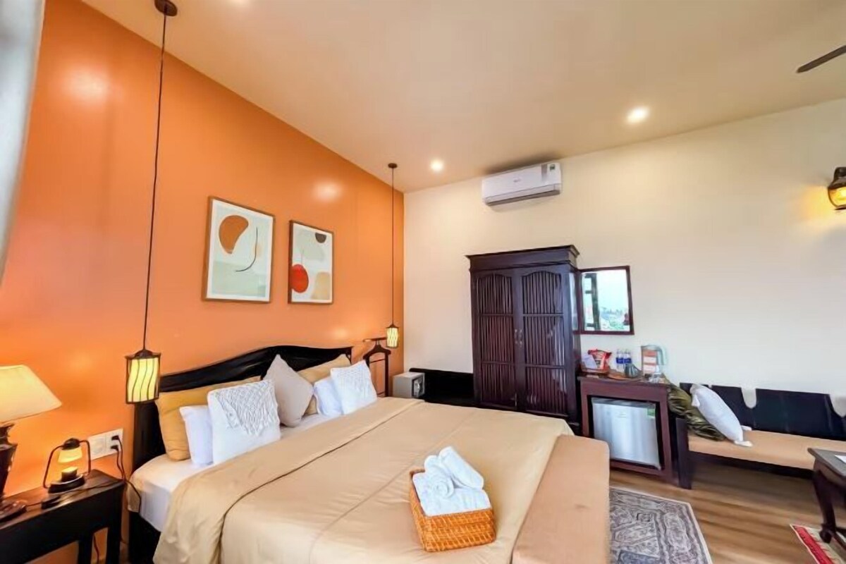 A hotel room with a bed, a nightstand, a lamp, a wall-mounted air conditioner, a wardrobe, and a small table with a lamp.