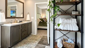 A modern bathroom with a large mirror, wooden vanity, and a shelf with towels and toiletries. - KY Lakeshore Retreat -Waterfront Views, Dock, Deck, Large Parking -NEW 2024 (New Concord)