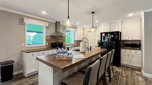 A modern kitchen with a central island, white cabinetry, a black refrigerator, and pendant lighting. - KY Lakeshore Retreat -Waterfront Views, Dock, Deck, Large Parking -NEW 2024 (New Concord)
