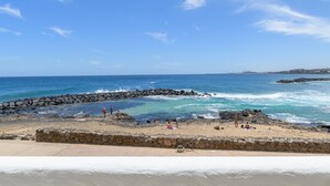 Una playa con un muro de piedra, cielo azul despejado y mar tranquilo.