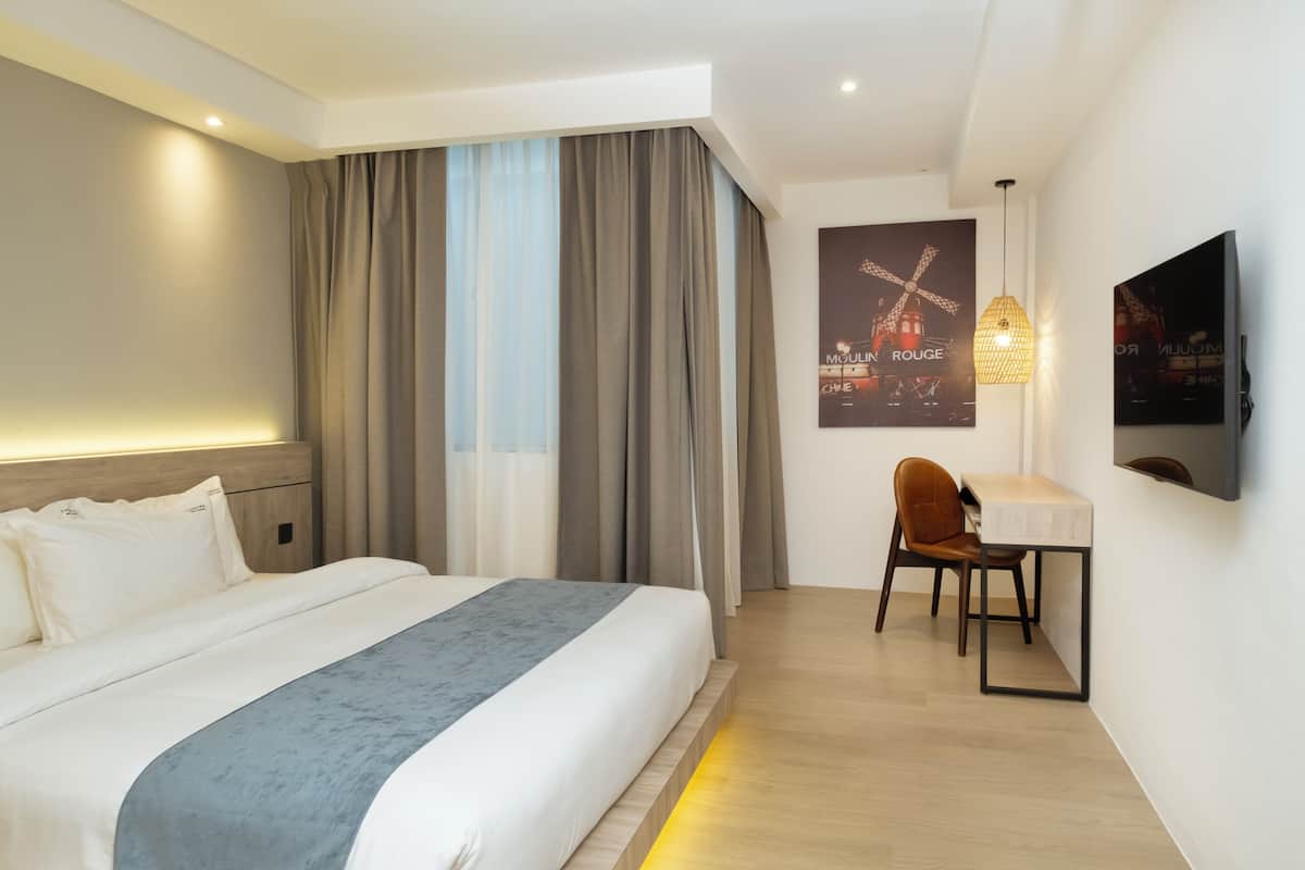 A hotel room with a bed, a desk, a chair, a television, and a wall-mounted artwork.