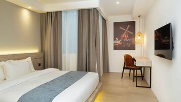 A hotel room with a bed, a desk, a chair, a television, and a wall-mounted artwork.