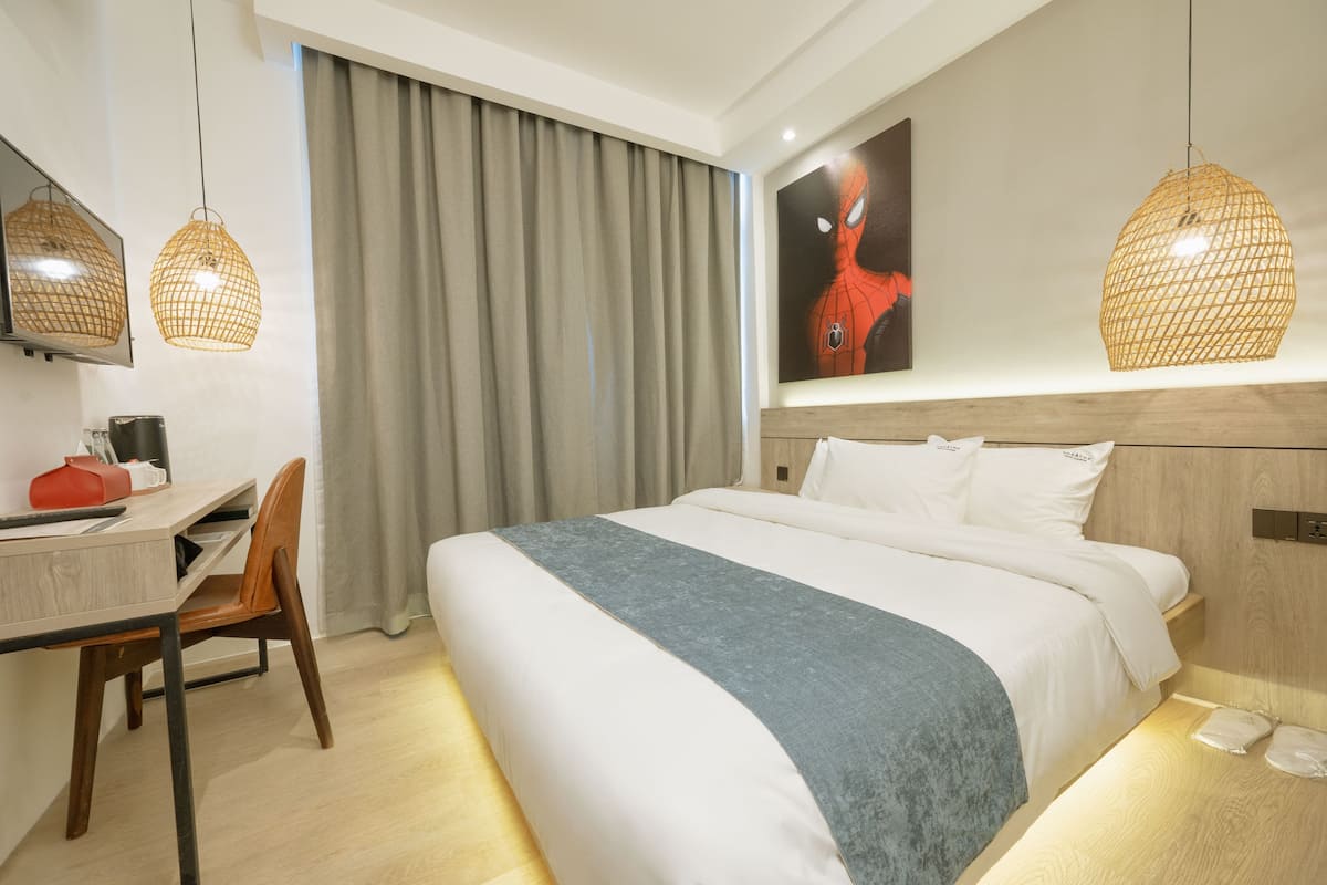 A hotel room with a large bed, a desk with a chair, a wardrobe, and a painting on the wall.