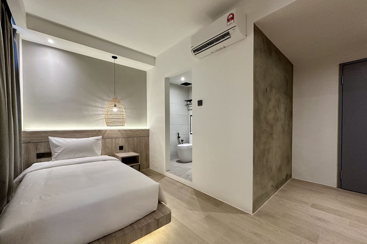 A modern hotel room with a large bed, a bedside table, a hanging light fixture, and an air conditioning unit.