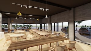 Un espacio interior amplio con varias mesas de madera y sillas de mimbre, grandes ventanales que ofrecen vistas de coches aparcados y vegetación exterior.