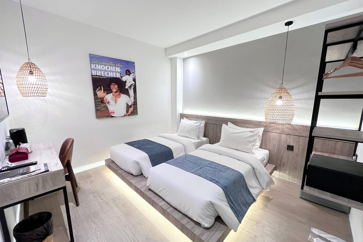 A modern hotel room with two beds, a desk, and a poster on the wall.