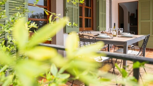Un espace extérieur abrité, aménagé pour les repas, avec une table pour deux, entouré de volets verts et surmonté d’un toit de chaume.