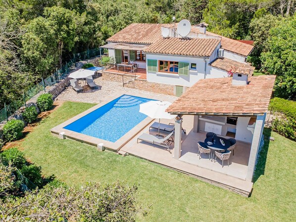 Uma casa de dois andares com piscina, área de estar externa e muro de pedra.