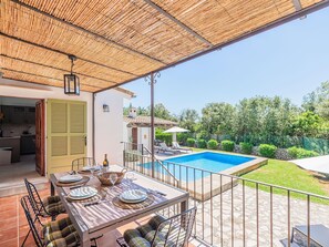 Uma área externa coberta com piscina, mesa de jantar posta e vista para o quintal.
