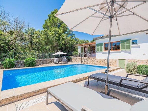A swimming pool with lounge chairs and an umbrella, surrounded by greenery and a stone wall. - Villa Can Bon Jesus by SunVillas Mallorca (Pollença)