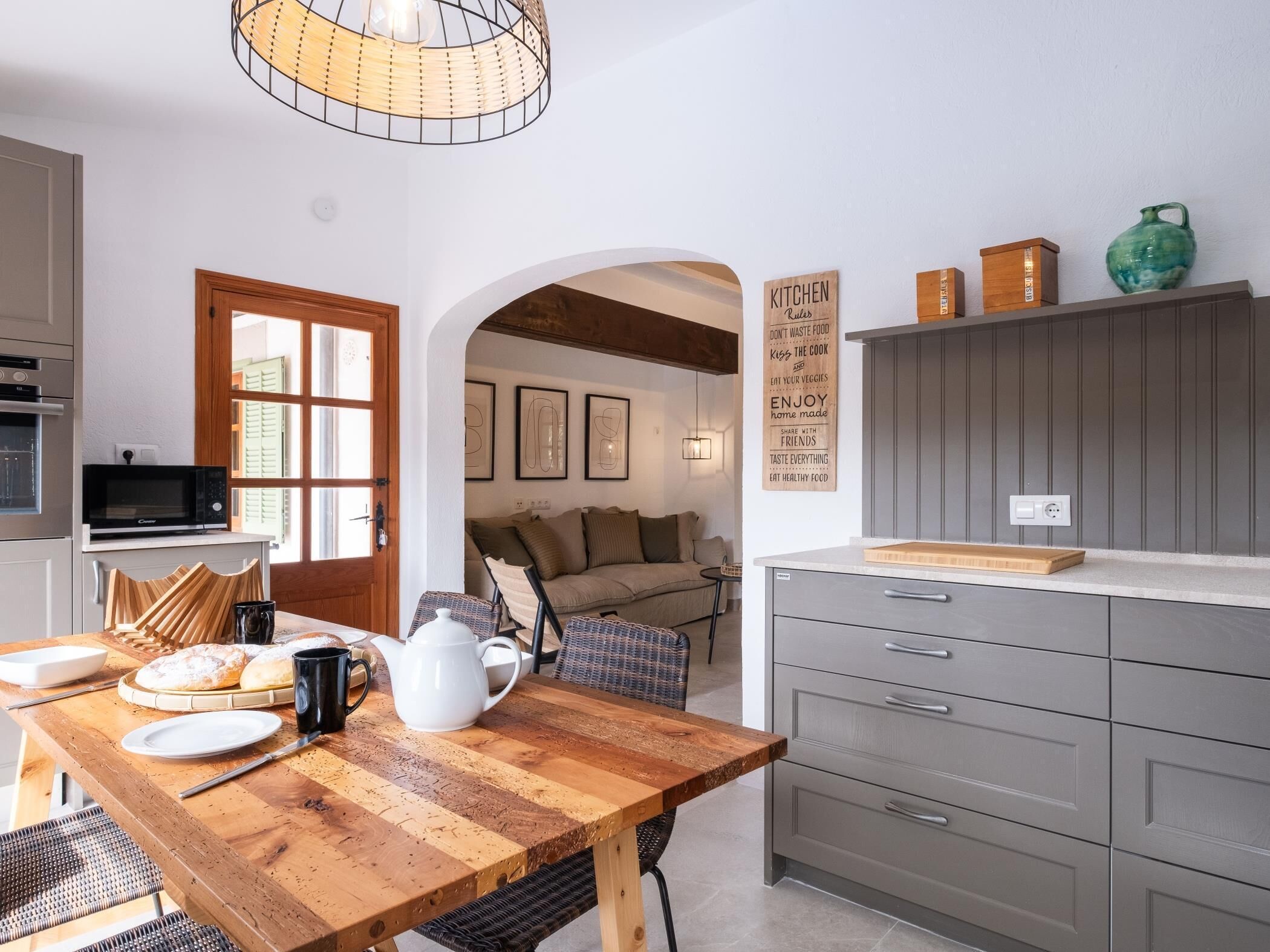 A modern kitchen with a wooden table, a microwave, and a sign with kitchen rules.