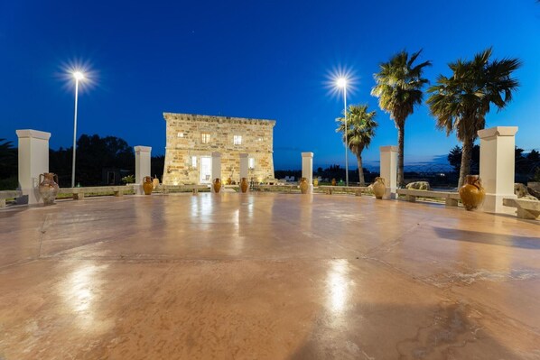 A stone building with columns, palm trees, and vases in an open area.