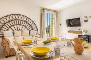 A dining area with a wicker sofa, a metal headboard, and a table set with yellow bowls, wine glasses, and a pitcher. - Villa Turris - Alliste ,Apulia (Alliste)