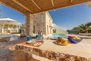 Colazione a bordo piscina con architettura in pietra, una piscina e palme.