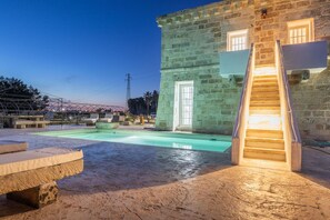 Un edificio in pietra con una scalinata che conduce a una porta, una piscina e un'area relax all'aperto.