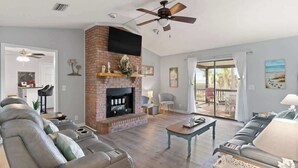 A living room with a fireplace, leather sofas, a coffee table, and a ceiling fan. - Marsh and Ember Cottage (Brunswick)