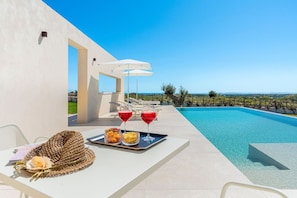 A poolside area with a view of the sea, a white table with a tray of snacks and drinks, and a woven basket with a rose. - Villa Mora - Finocchiara ,Sicily (Rosolini)