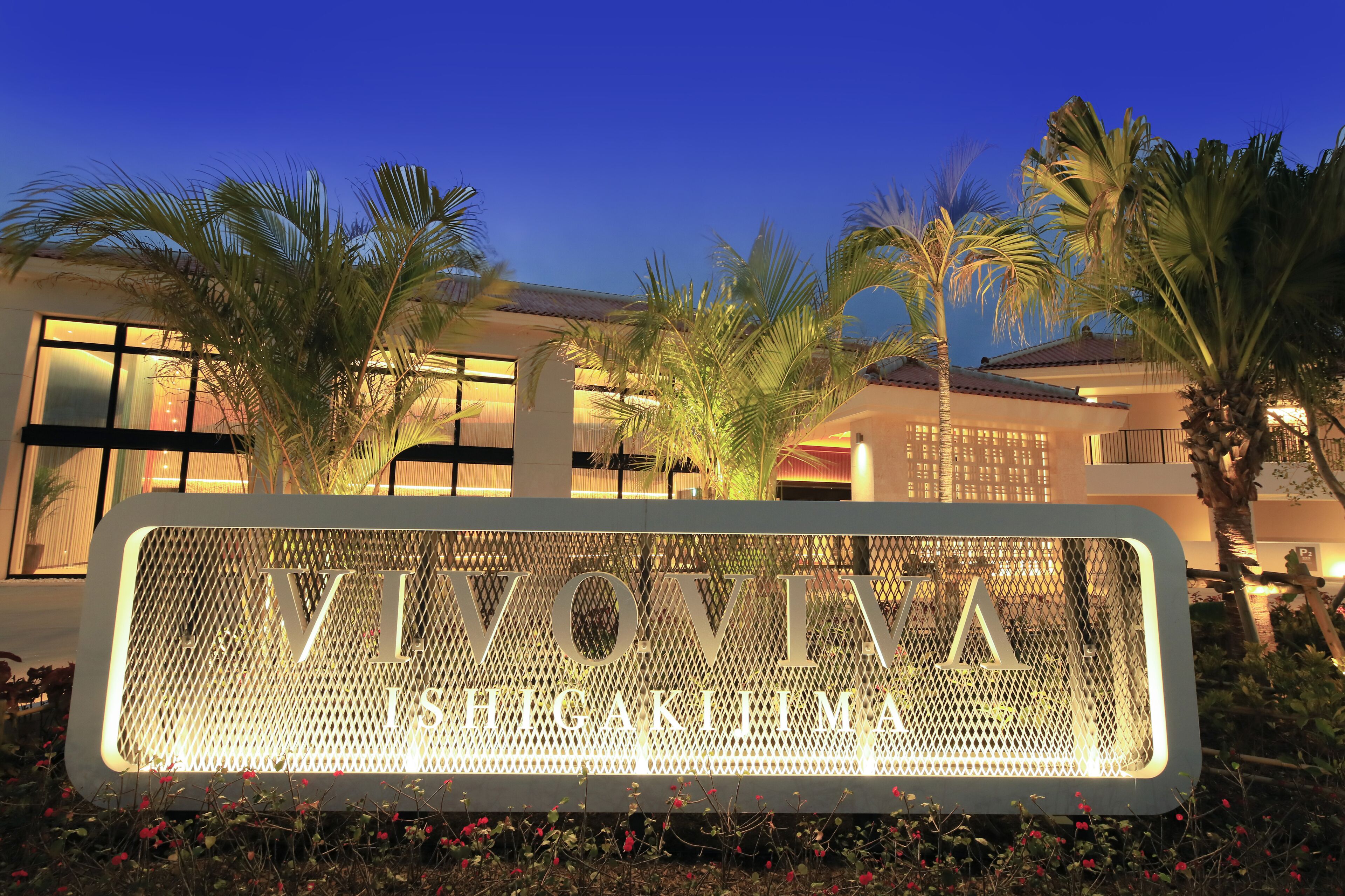 A sign with "VIVONIA" and "HIGAKIMIYA" written on it, surrounded by palm trees and a building with large windows.