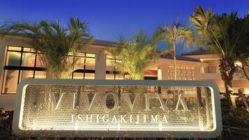 A sign with "VIVONIA" and "HIGAKIMIYA" written on it, surrounded by palm trees and a building with large windows.