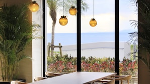 A dining area with a view of the sea, featuring a wooden table and chairs, hanging spherical lights, and potted plants. - VIVOVIVA ISHIGAKIJIMA (Ishigaki)