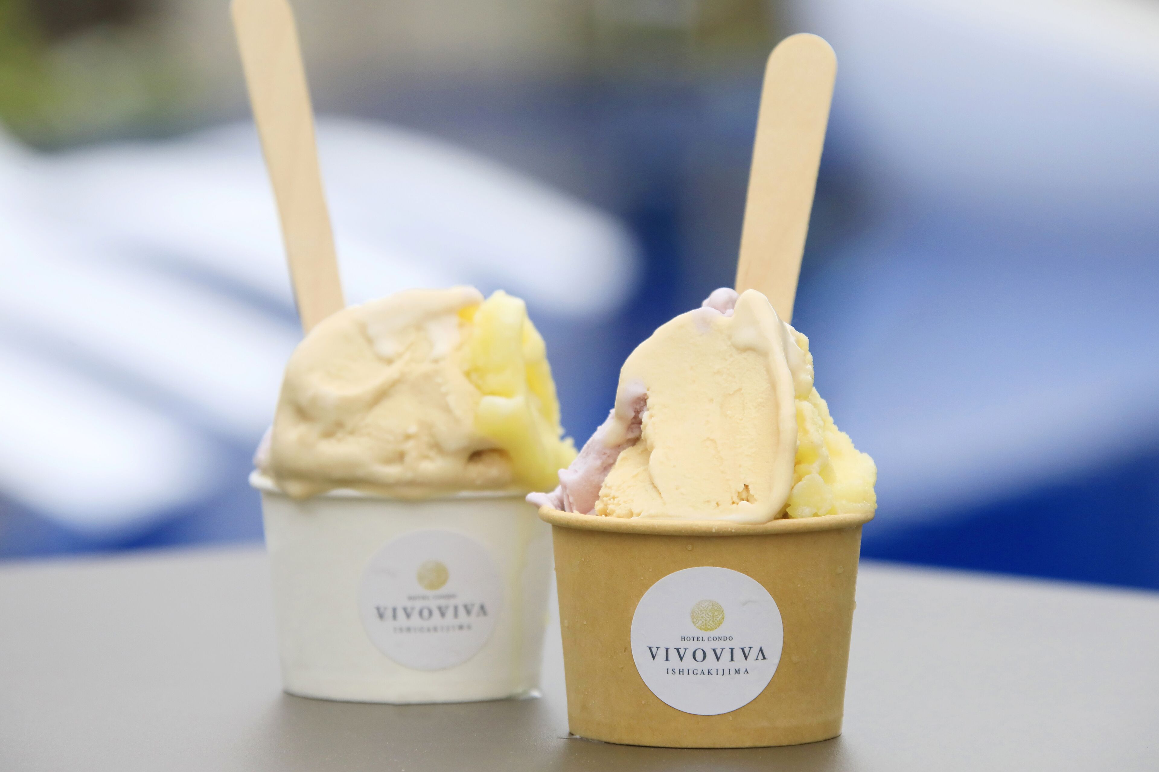 Two cups of ice cream with wooden sticks, labeled 'VIVOVIVA', on a table.