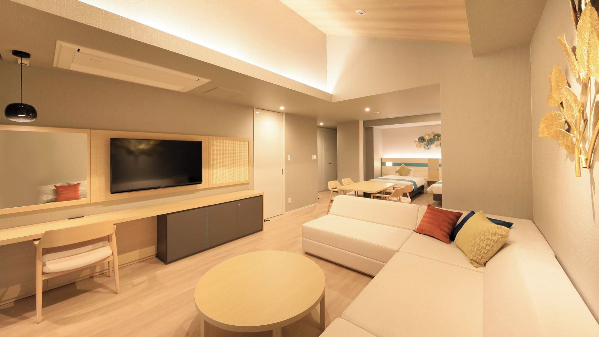 A modern living room with a flat-screen TV, a sofa, a dining table, and a kitchen area.