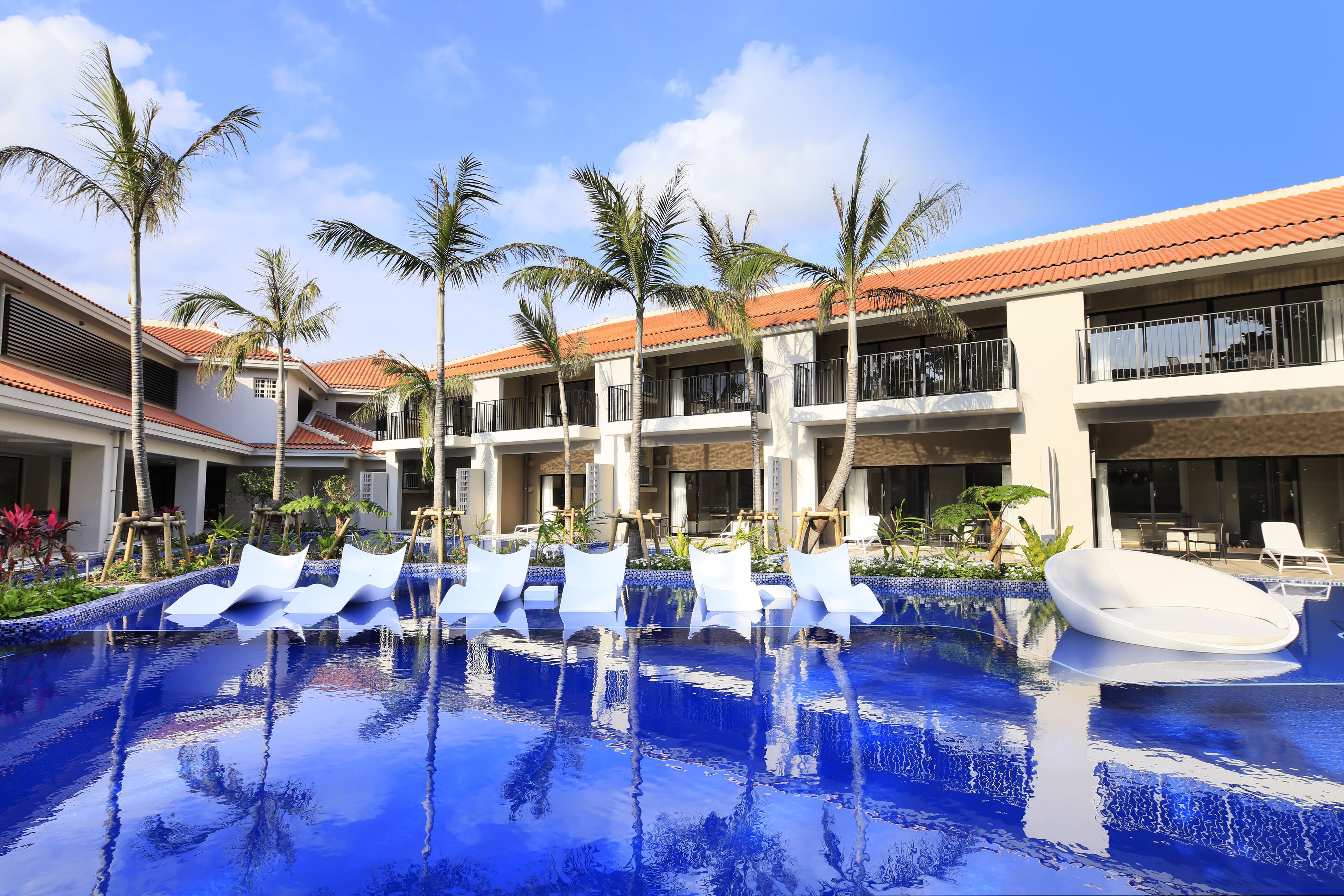 Uma área de piscina de hotel com várias espreguiçadeiras e palmeiras.