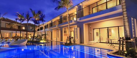 Un hotel moderno con piscina, palmeras y un espacio exterior bien iluminado.