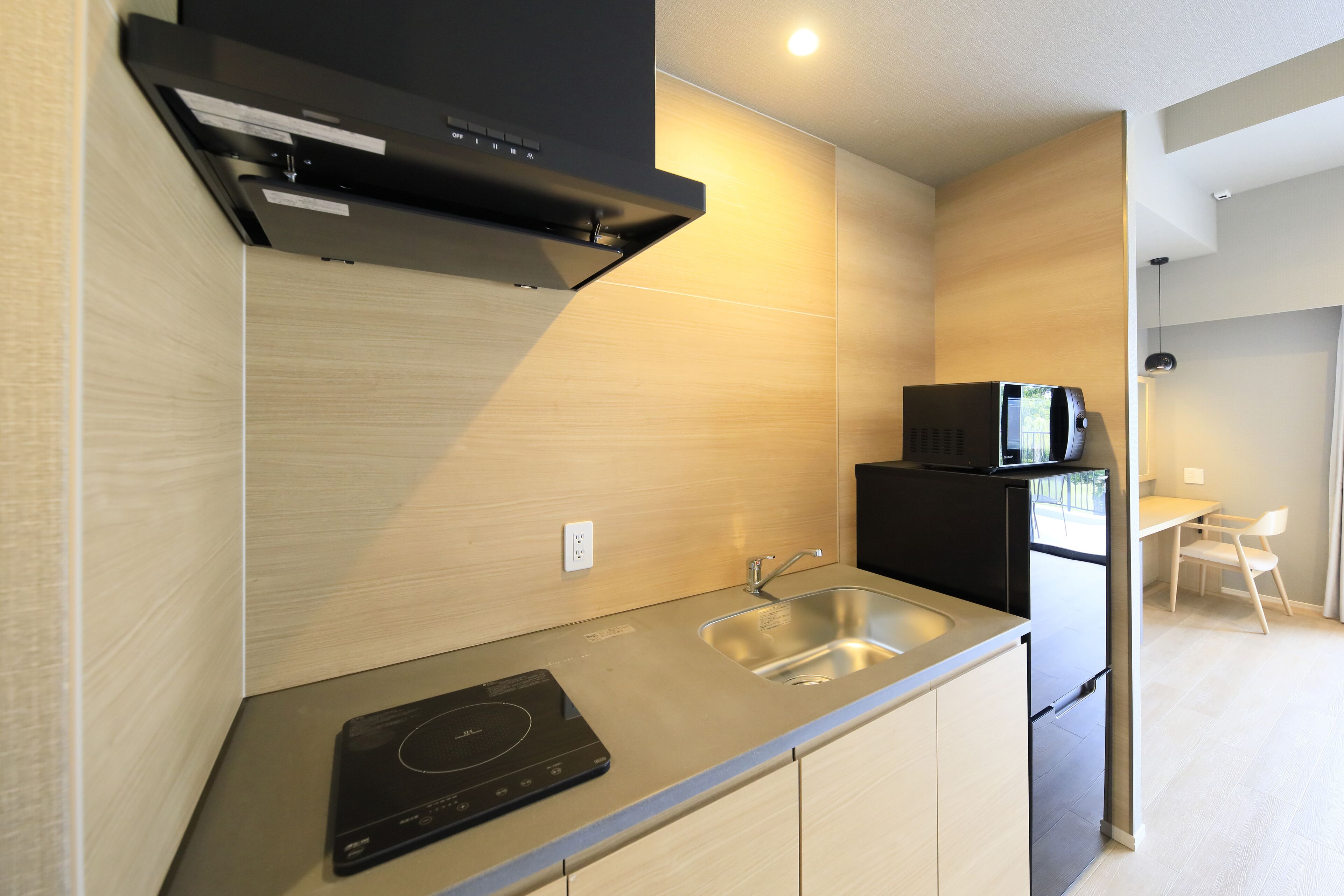 A modern kitchen with a built-in induction cooktop, stainless steel sink, and black microwave.