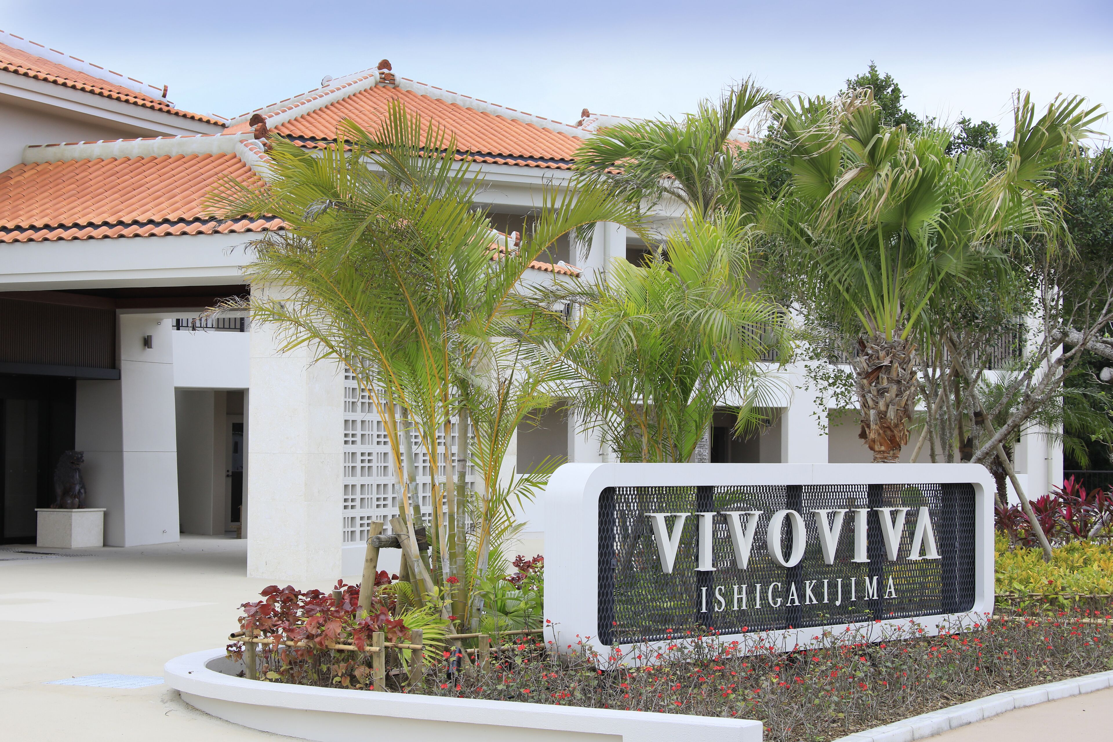Un letrero que dice 'VIVOVIVA ISHIGAKIJIMA' con un edificio al fondo.