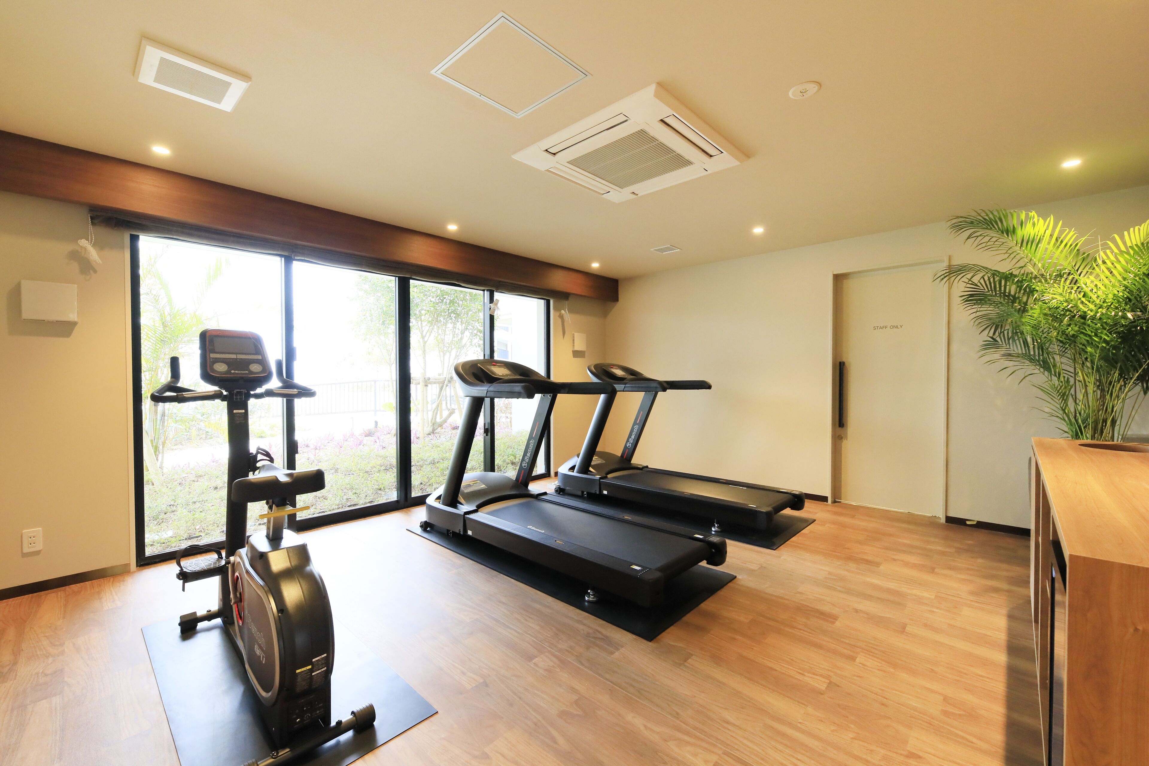 Una palestra con due tapis roulant, un ellittica e una grande finestra vista su spazi verdi.