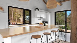Una cocina moderna con una isla grande, taburetes de bar y vistas al bosque.