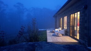 Un patio moderno al aire libre con suelo de piedra, sillas blancas y vistas del paisaje circundante.