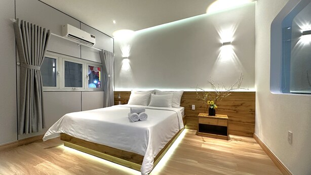 Quarto de hotel moderno com uma cama grande, cabeceira de madeira e mesa de cabeceira com um vaso de flores.