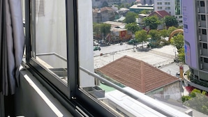Paisagem urbana vista pela janela, com edifícios altos, céu claro e rua abaixo.