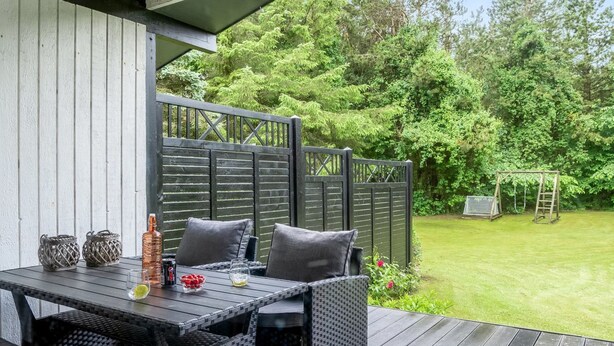 Eine Terrasse im Freien mit Tisch und Stühlen, umgeben von einem Holzzaun und üppiger Bepflanzung.