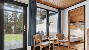 Ein gemütliches Zimmer mit Holzbalkendecke, einem Esstisch mit Stühlen, einem Bett und einem Fenster mit Vorhängen.
