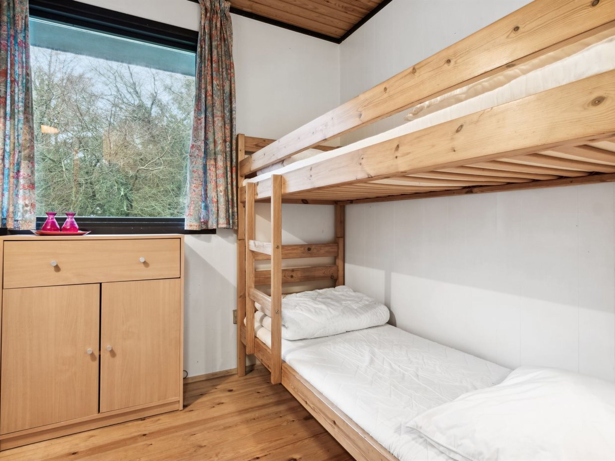Une chambre avec un lit superposé, une armoire en bois et une fenêtre avec des rideaux.