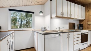 Eine moderne Küche mit weißen Schränken, einem Geschirrspüler, einer Spüle und einem Fenster mit Blick auf Bäume.