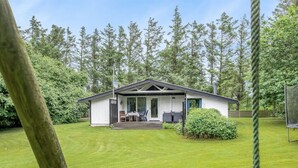 Ein kleines, eingeschossiges Haus mit Veranda, umgeben von einem gepflegten Rasen und hohen Bäumen.