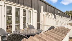 Eine Terrasse mit rundem Tisch, Korbstühlen, einer Getränkflasche und einem Glas.