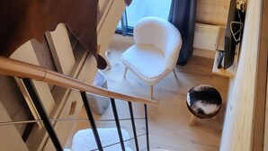 Un escalier menant à une pièce où se trouvent une chaise blanche, un chien noir et un plancher en bois.