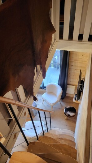 Una escalera que lleva a una habitación con una silla blanca, un perro negro y un suelo de madera.