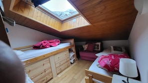 Une chambre de dortoir avec des lits superposés, une commode en bois, un bureau et une lucarne.