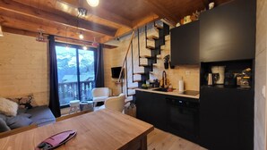 L’intérieur chaleureux d’un chalet avec une table à manger en bois, un canapé, une cuisine dotée d’un plan de travail noir et un escalier menant à un balcon.