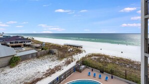 A beach view from a balcony with a pool, lounge chairs, and a building with a sign reading "CLUB LA VELA".
