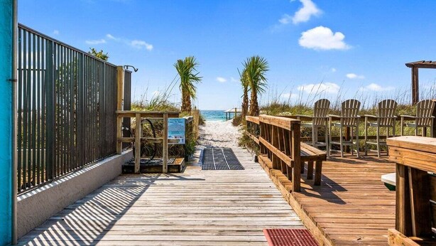 A wooden boardwalk leading to a beach with palm trees and beach chairs.