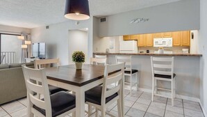 A modern kitchen with white cabinets, a microwave, and a refrigerator. There is a dining area with a wooden table and white chairs.